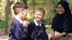 Three students laughing together in an outdoor play area.